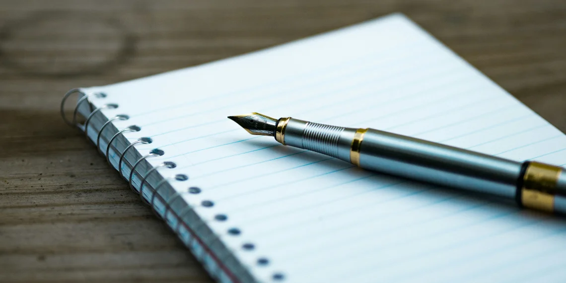 Tilted open ring notebook on an empty page, adorned with a classy fountain pen, symbolizing the artful process of writing.